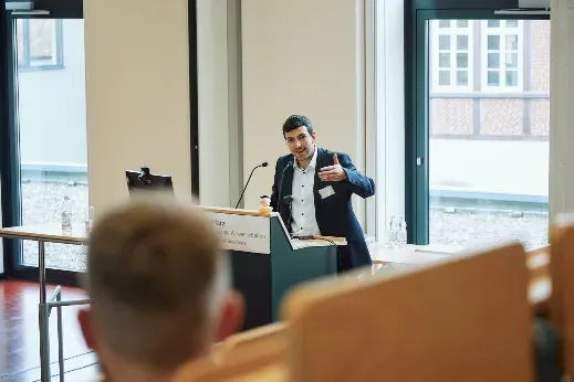 Vortragender am Rednerpult, gestikulierend, im Hintergrund der Innenhof der Hochschule.